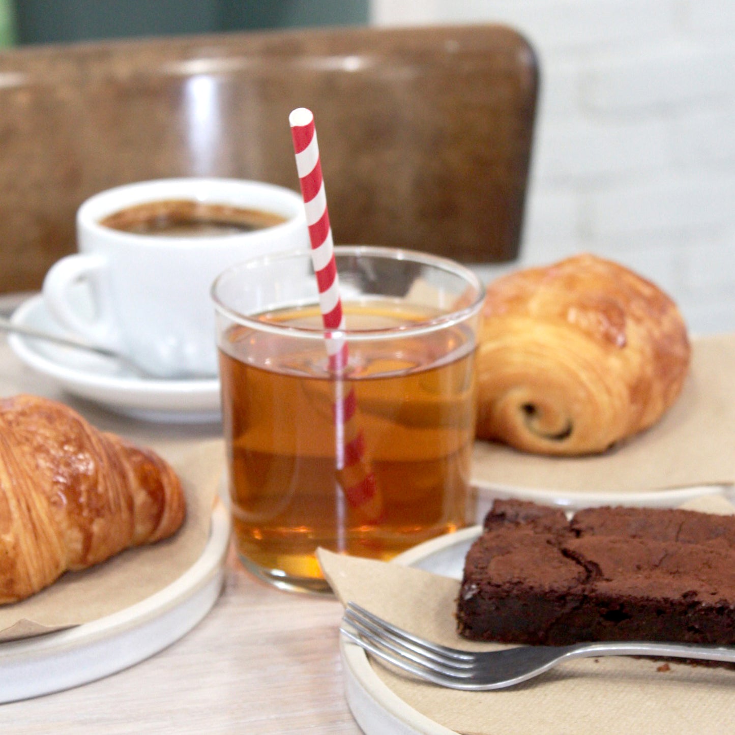 A glass of apple juice with a red and white stripey straw surrounded by baked goods