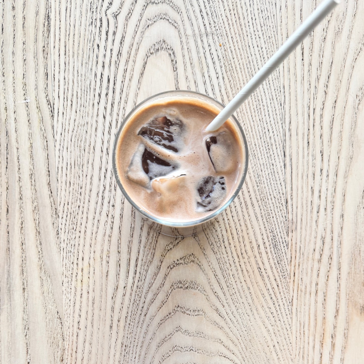An iced Mocha in a glass on a wooden table with a straw